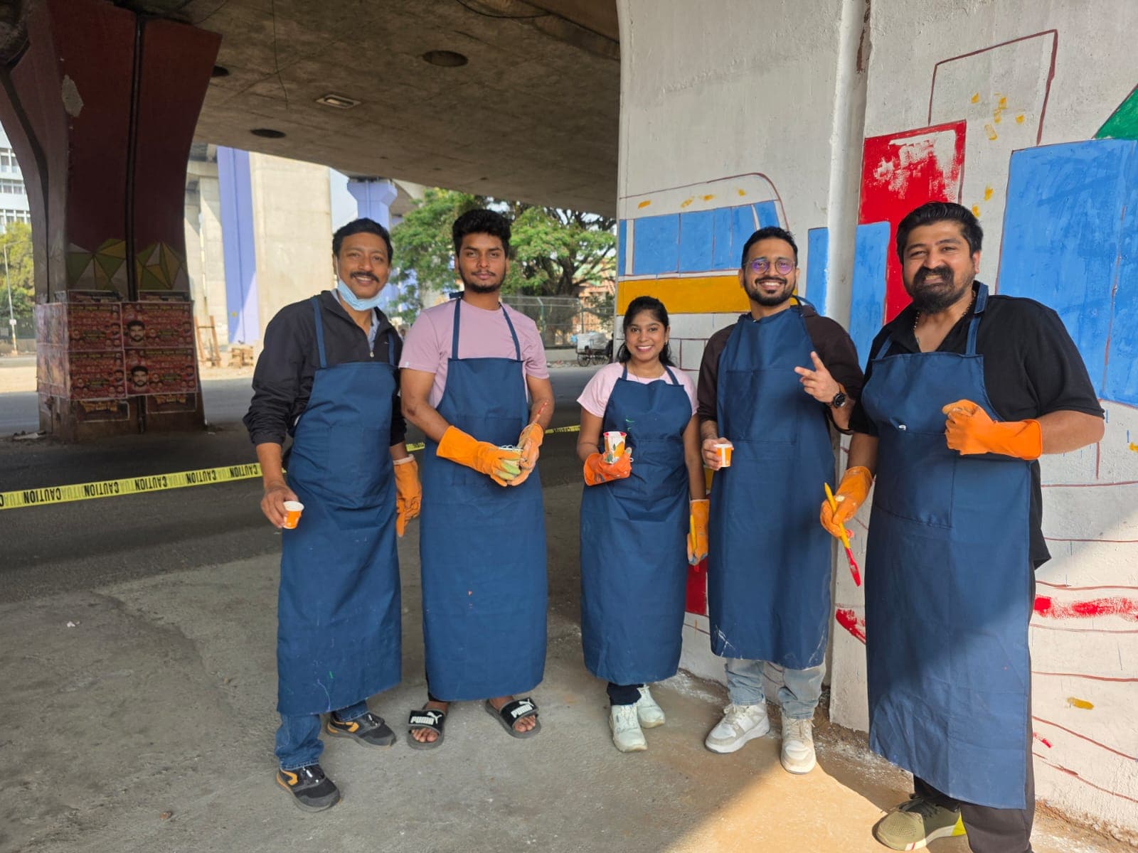 Volunteers wearing gloves beside a freshly painted underpass pillar